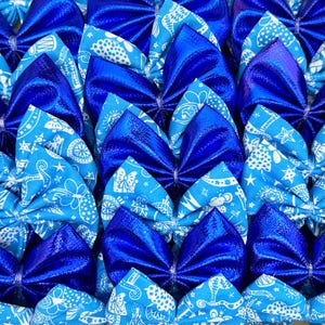 May include: A close-up shot of numerous blue fabric bows. Some are a solid, shiny blue, while others display a light blue paisley pattern. The bows are tightly packed, forming a textured surface.