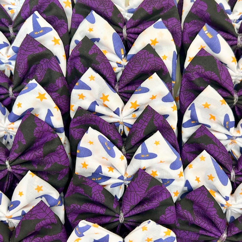 Peut inclure: Une collection de n&oelig;uds pour cheveux sur le th&egrave;me d'Halloween. Les n&oelig;uds pr&eacute;sentent divers motifs, notamment des chapeaux de sorci&egrave;re, des &eacute;toiles et des toiles d'araign&eacute;es. La palette de couleurs comprend le violet, le noir, le blanc et le jaune.
