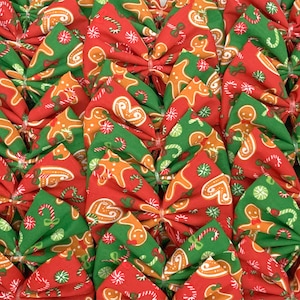 May include: A collection of handmade Christmas bows featuring a red and green gingerbread man print. The bows are made of fabric and are perfect for adding a festive touch to any gift or decor.