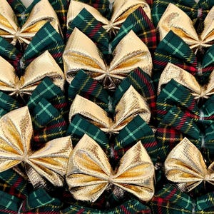 May include: A close-up shot of several gold metallic bows arranged on green and red tartan fabric. The bows are closely packed together, forming a decorative pattern. The bows are a shiny gold colour.