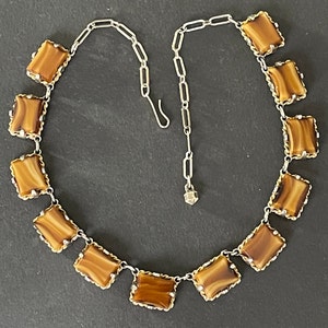 May include: A brown and gold necklace with a silver chain and square-shaped brown stones.