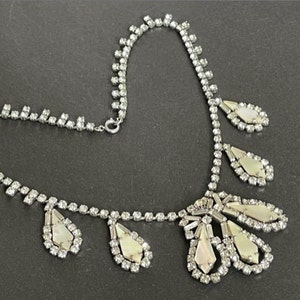 May include: A silver necklace with a delicate chain and a large, ornate pendant. The pendant is made of white iridescent stones and is shaped like a teardrop. The necklace is a vintage style and would be a beautiful addition to any jewelry collection.