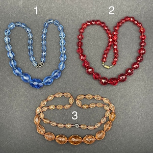 Puede incluir: Tres collares de cuentas de vidrio, uno azul, uno rojo y uno ámbar. Los collares están numerados del 1 al 3.