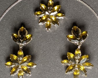 Puede incluir: Un conjunto de joyas doradas con un colgante y pendientes. El colgante y los pendientes presentan un diseño floral con múltiples piedras amarillas.