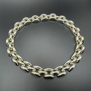 Puede incluir: Un collar plateado con un diseño de eslabones. El collar está compuesto por múltiples filas de eslabones de forma ovalada, creando una pieza audaz y elegante. Los eslabones tienen un acabado pulido.