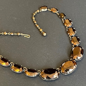 Könnte beinhalten: Eine Vintage-Halskette mit großen, oval geformten, facettierten braunen Steinen, die in goldfarbenem Metall gefasst sind. Die Halskette hat eine filigrane Kette mit kleineren, runden Perlen und einem Hakenverschluss. Die Steine glänzen.