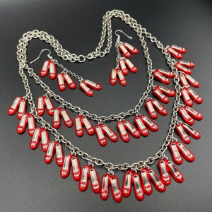 May include: A silver necklace with multiple strands and red shoe charms. The necklace is layered and features a variety of red shoe charms, some with bows and some with buckles.