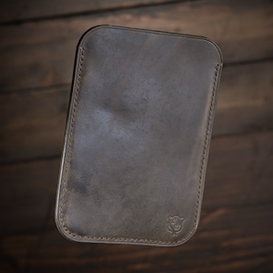 Puede incluir: Una funda de teléfono de cuero marrón con un borde cosido y un pequeño logotipo en la parte inferior.