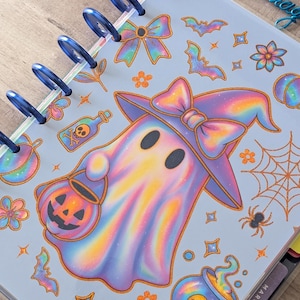 May include: A disc-bound planner with a light blue cover featuring a holographic ghost wearing a witch hat and holding a jack-o'-lantern bucket. The cover design includes orange and holographic icons of bats, spiders, webs, and potion bottles.