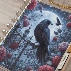 May include: A disc-bound planner featuring a cover illustration of a black raven perched on an ornate iron gate against a full moon background, surrounded by deep red roses. The planner includes gold-colored discs and side tabs labeled September and December.