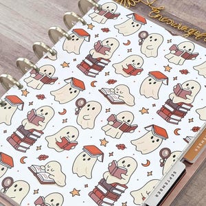 May include: A disc-bound planner cover featuring a repeating pattern of cream-colored ghosts reading books, holding magnifying glasses, and balancing on stacks of books, interspersed with small orange stars, crescent moons, and autumn leaves.