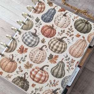 May include: A disc-bound planner featuring a cream-colored cover with a repeating pattern of pumpkins in various shades of orange, green, and brown, accented by small leaves and berries. The planner includes visible plastic discs and tabbed dividers.