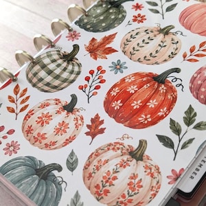 May include: A disc-bound planner cover featuring a white background with a repeating pattern of pumpkins in various colors including orange, green, and cream, accented with floral motifs, autumn leaves, and berries, with a September tab visible.