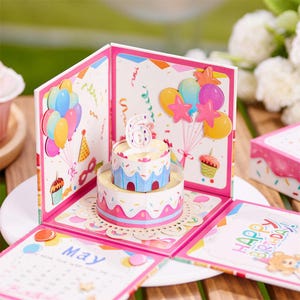 May include: A pop-up birthday greeting card featuring a two-tiered paper cake with a number 6 topper. The card displays colorful illustrations of balloons, confetti, and a cupcake. One panel shows a calendar for May, and another reads Happy Birthday.