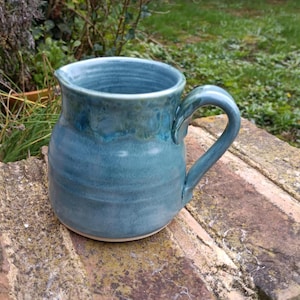 Può includere: Un'anfora in ceramica blu con un bordo bianco e un manico. L'anfora ha una finitura testurizzata e smaltata.