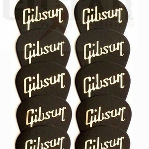 Könnte beinhalten: Zehn schwarze Gitarrenplektren mit dem Wort "Gibson" in weiß auf jedem Plektrum.
