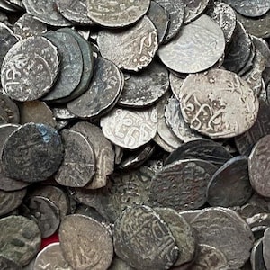 May include: A large pile of silver coins with intricate designs and Arabic script. The coins are arranged in a random pattern, creating a textured surface.