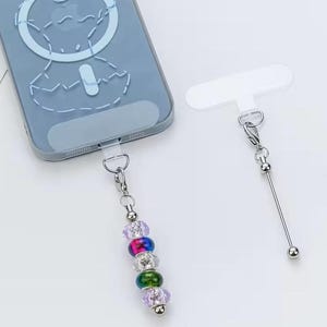 May include: A light blue smartphone case with a circular magnetic design, featuring a silver-toned metal tether tab attached to a beaded charm. The charm consists of five spherical beads in purple, pink, clear, green, and light purple colors.