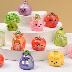 May include: A collection of colorful, miniature vegetable figurines with smiling faces. The figurines include a broccoli, onion, tomato, and pepper. The figurines are displayed on a tiered white platform.