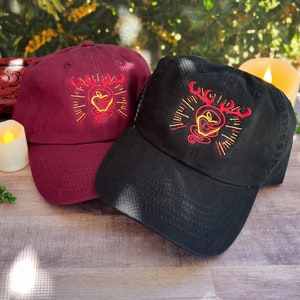 Peut inclure: Deux casquettes de baseball avec des motifs brodés. Une casquette est bordeaux avec un motif jaune et rouge. L'autre casquette est noire avec un motif jaune et rouge.