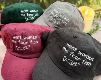Peut inclure: Quatre casquettes de baseball avec le texte "want women me fear fish" et un petit dessin de poisson brodé sur le devant. Les casquettes sont en vert, gris, bordeaux et noir.