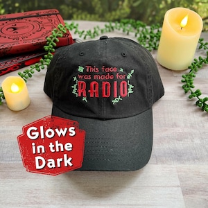 Könnte beinhalten: Schwarze Baseballkappe mit grüner und roter Stickerei, auf der "This face was made for RADIO" steht. Die Kappe leuchtet im Dunkeln.