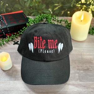 Puede incluir: Gorra de béisbol negra con el texto bordado "Bite me (Please)" en rojo y blanco. La gorra tiene una visera curva y un diseño clásico de seis paneles, perfecta para uso casual.