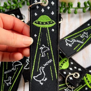 An embroidered jet tag keychain of two geese being abducted by aliens
