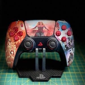 Könnte beinhalten: Ein schwarzer PlayStation 5-Controller mit einem benutzerdefinierten Design, das eine Frau in einem roten Outfit und den Text "No More Mutants" zeigt. Der Controller befindet sich auf einem schwarzen Ständer mit einem PlayStation-Logo.