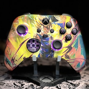 May include: A custom Xbox controller with a yellow, orange and blue anime-style design featuring a character with spiky blonde hair. The controller has purple LED lights around the buttons.
