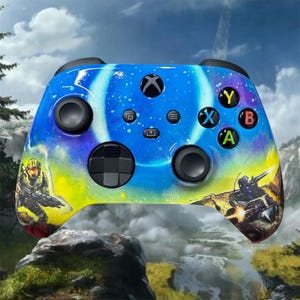 Op de afbeelding: Aangepaste Xbox-controller met een ruimtethema-ontwerp in blauw, geel en paars. De controller heeft zwarte knoppen en joysticks en toont afbeeldingen van een soldaat en een voertuig. Het Xbox-logo is zichtbaar.