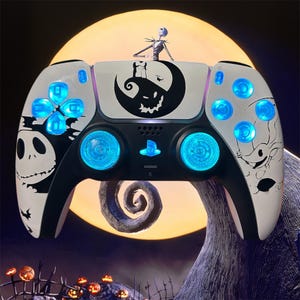 Puede incluir: Un mando de videojuegos personalizado en blanco y negro con personajes de Pesadilla antes de Navidad. El mando tiene botones y joysticks azules brillantes, con gráficos temáticos de Jack Skellington.