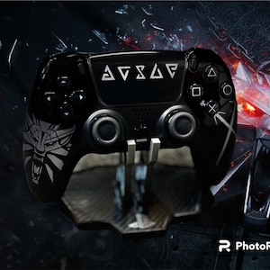 May include: Black PlayStation controller with white symbols and a wolf emblem. The controller is on a stand. The controller has the text symbols on the top. The background is dark with a wolf image.