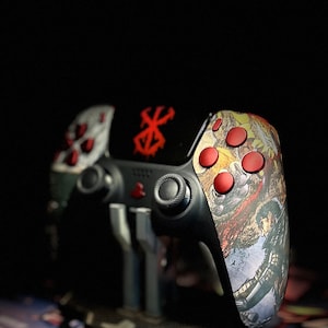 Może przedstawiać: Czarny i czerwony kontroler do gier wideo z niestandardowym wzorem przedstawiającym czerwoną i białą czaszkę i skrzyżowane kości. Kontroler znajduje się na stojaku i ma fakturowaną powierzchnię.