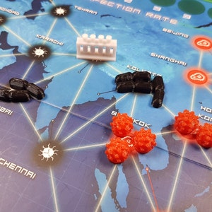 May include: A game board with a map of the world, showing cities such as Mumbai, Karachi, and Beijing. There are red and black game pieces on the board, as well as a white plastic building.