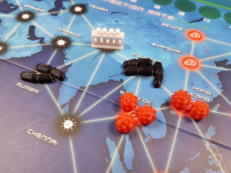May include: A game board with a map of the world, showing cities such as Mumbai, Karachi, and Beijing. There are red and black game pieces on the board, as well as a white plastic building.