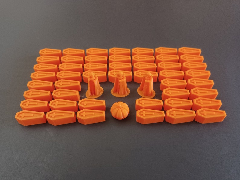 May include: A set of 36 orange plastic coffin-shaped game pieces and 5 orange plastic Halloween-themed game pieces, including a pumpkin, a ghost, and a witch.