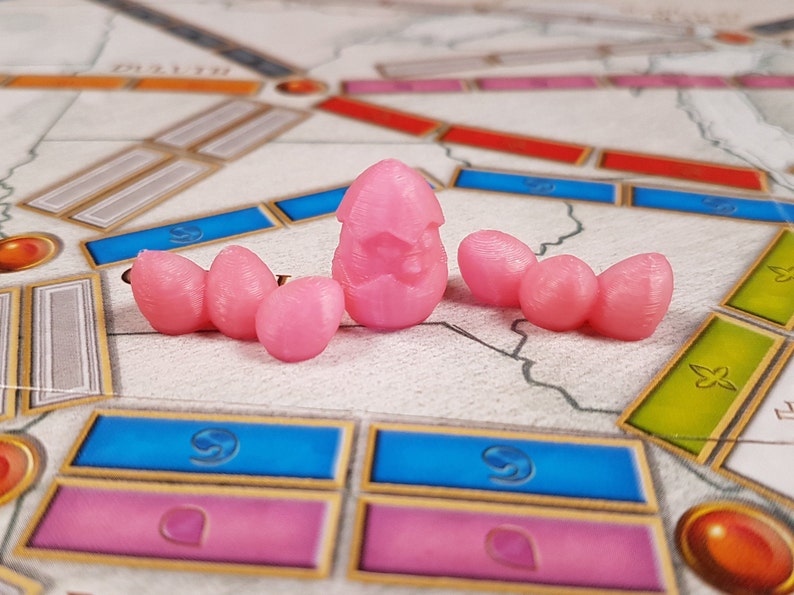 Puede incluir: Cinco piezas de juego de color rosa, una con un dise&ntilde;o de estrella, sobre un tablero de juego con casillas azules y rosas.