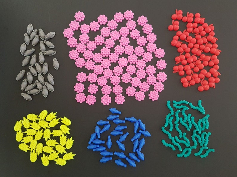 May include: Assortment of colorful plastic game pieces in various shapes, including flowers, fish, leaves, and cherries. The pieces are arranged in groups on a black background.