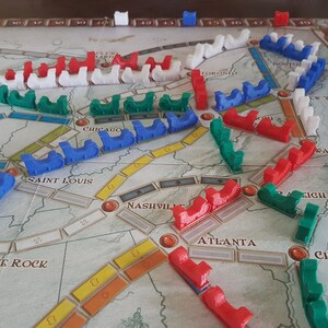 May include: A game board with red, blue, green, and white train pieces. The board shows the United States with cities and routes.