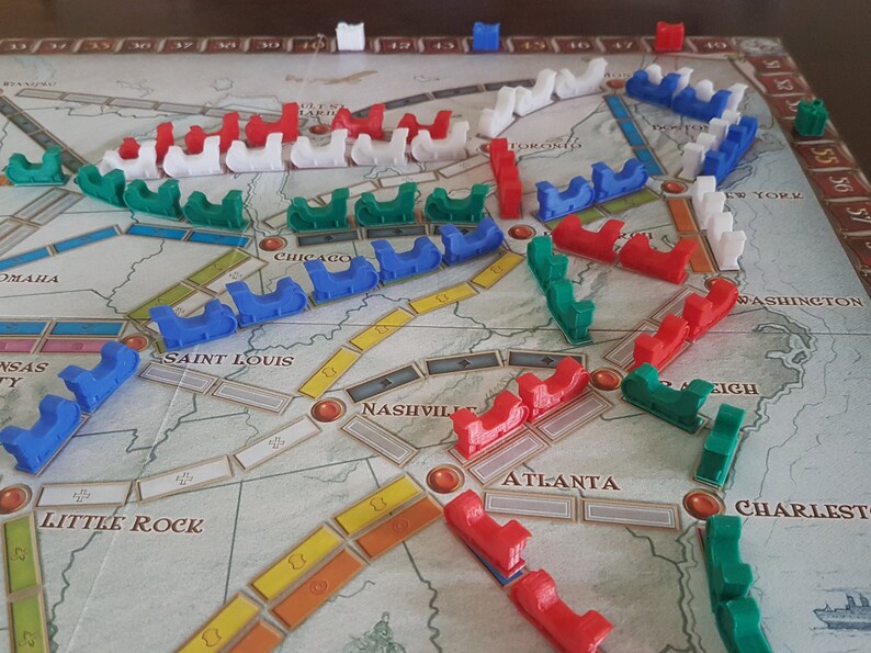May include: A game board with red, blue, green, and white train pieces. The board shows the United States with cities and routes.