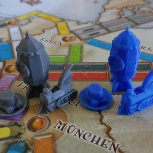 May include: Two sets of miniature train and airship game pieces. One set is gray and the other is blue. Each set includes a train, an airship, and a hat.