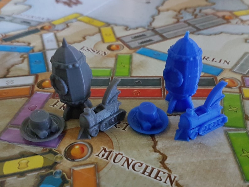 May include: Two sets of miniature train and airship game pieces. One set is gray and the other is blue. Each set includes a train, an airship, and a hat.