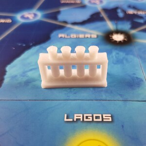 May include: White plastic test tube rack with four test tubes. The rack is sitting on a blue and white game board.
