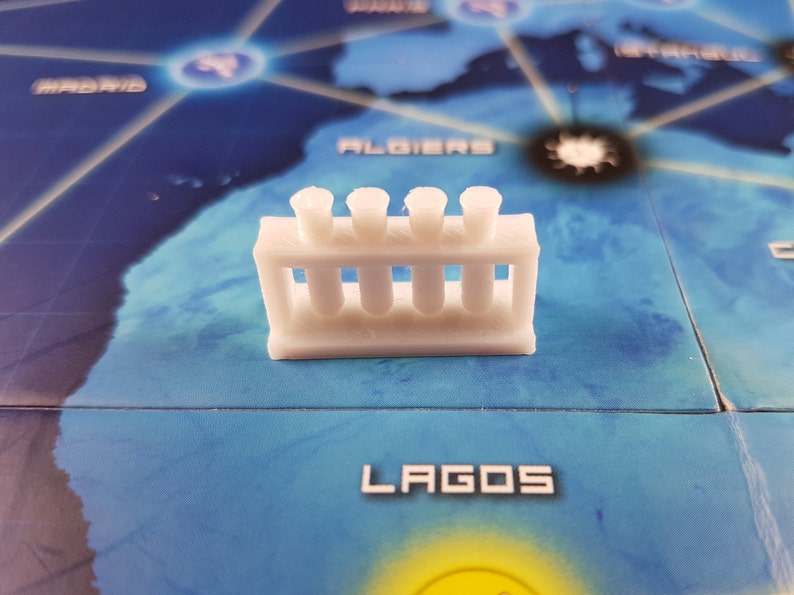 May include: White plastic test tube rack with four test tubes. The rack is sitting on a blue and white game board.