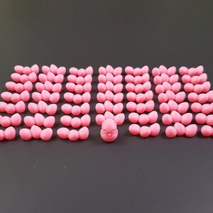 Puede incluir: Un pollito de cer&aacute;mica rosa rodeado de 40 huevos de cer&aacute;mica rosa. Los huevos est&aacute;n dispuestos en filas de tres, con el pollito en el centro.