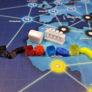 May include: A collection of colourful game pieces for a board game. The pieces include a white cube, a white test tube rack, a black cube, a black cylinder, a red cube, a red virus, a blue cube, a blue oval, a yellow cube, and a yellow virus.
