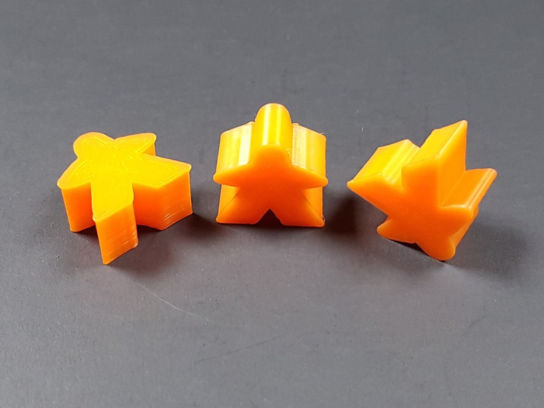 May include: Three orange plastic game pieces in the shape of a person, a star, and a five-pointed star.