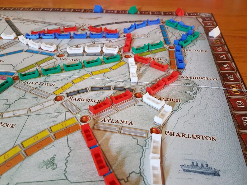 May include: A game board with different colored pieces on it. The board shows a map of the United States with cities labeled. The pieces are red, green, blue, and white.