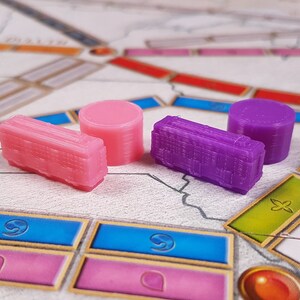 May include: Four game pieces for a board game. Two are pink and two are purple. The pink pieces are rectangular and the purple pieces are cylindrical.